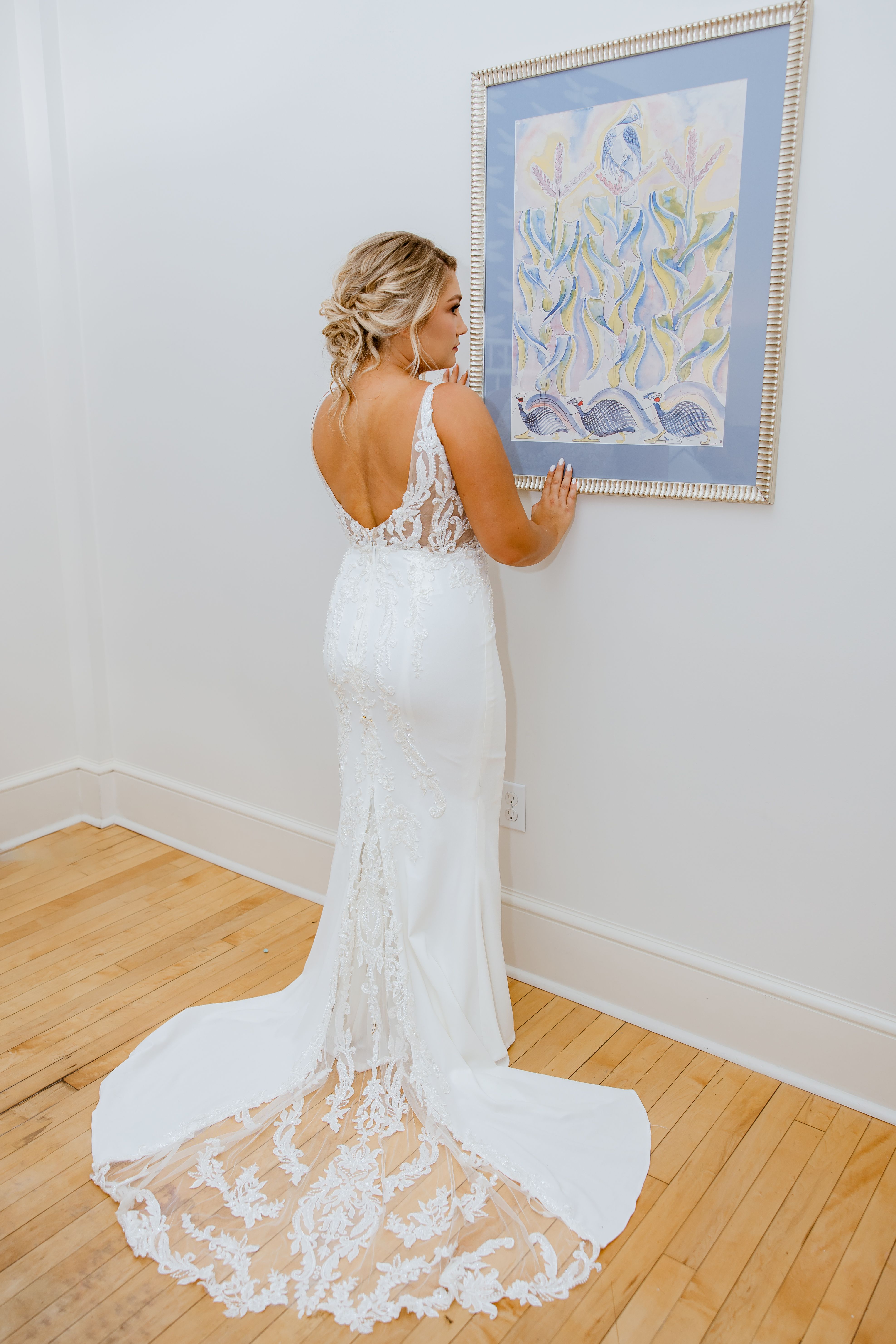 Bride seen from behind with a textured low updo, open lace back, and long lace train
